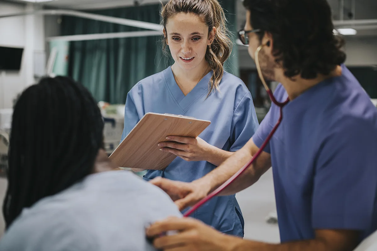 a student doctor holding a clipboard, speaking to a patient